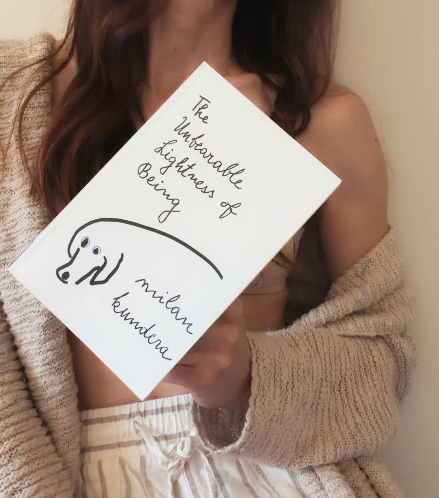 Close-up of a blogger's hands gently holding a copy of Milan Kundera’s The Unbearable Lightness of Being that came as a personal book recommendation.